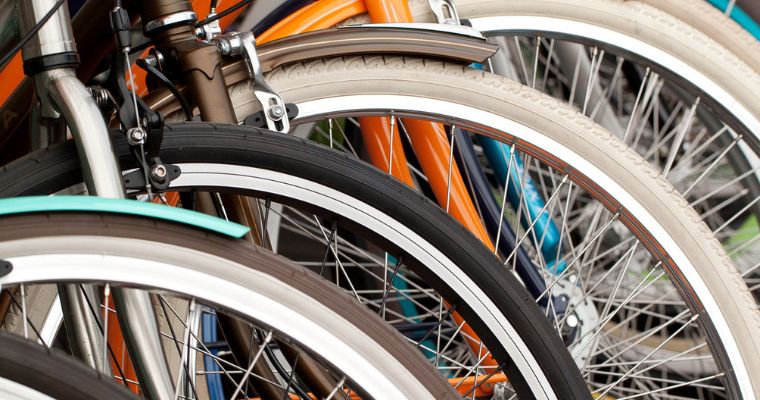 Gros plan sur plusieurs roues de vélo alignées, avec des cadres colorés et un mélange de pneus blancs et noirs, les rayons, jantes et fourches avant étant bien visibles.