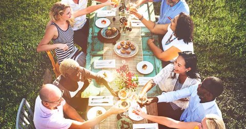 Groupe de personnes réunies autour d’une table en plein air, partageant un repas et trinquant dans une ambiance conviviale.